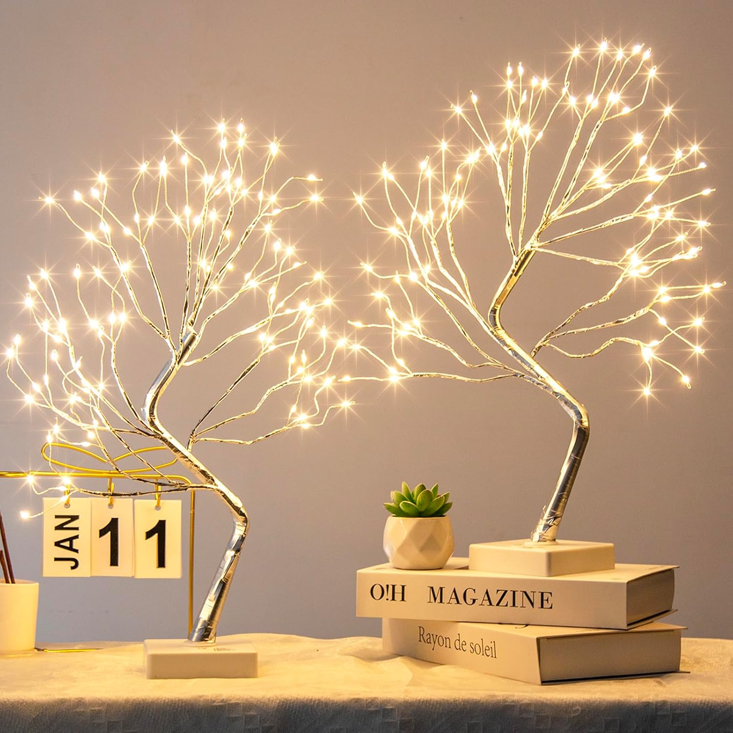 Decorative LED tree lights on books with a small plant and calendar in the background.